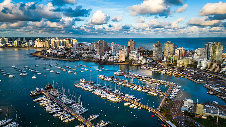 Drone shot revealing the picturesque coastal seaside city of Pun beautiful clouds on blue sky with uruguay skyline and boats